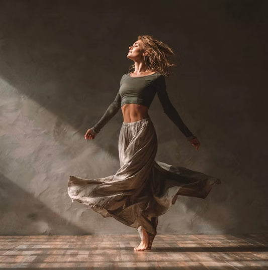 A person dancing gracefully in a soft, neutral-toned room, expressing fluid motion and freedom through movement.